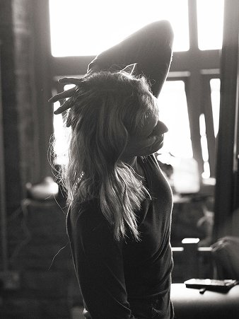 A black and white photo of Helen, founder and teacher at The Movement Retreat, in profile with her head tilted back and hand raised to her hair, backlit by a large studio window.